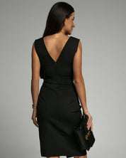 Donna in abito nero elegante con scollo a V, vista posteriore, tiene una borsa nera. Moda femminile, abbigliamento da ufficio, stile sofisticato.