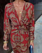 Abito rosso elegante con stampa floreale dorata, scollo a V profondo, maniche lunghe, accessori dorati, moda donna, stile sofisticato.