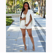 Donna in completo bianco elegante con occhiali da sole rosa, collana lunga dorata, tacchi beige, su viale alberato. Moda estiva, stile chic.