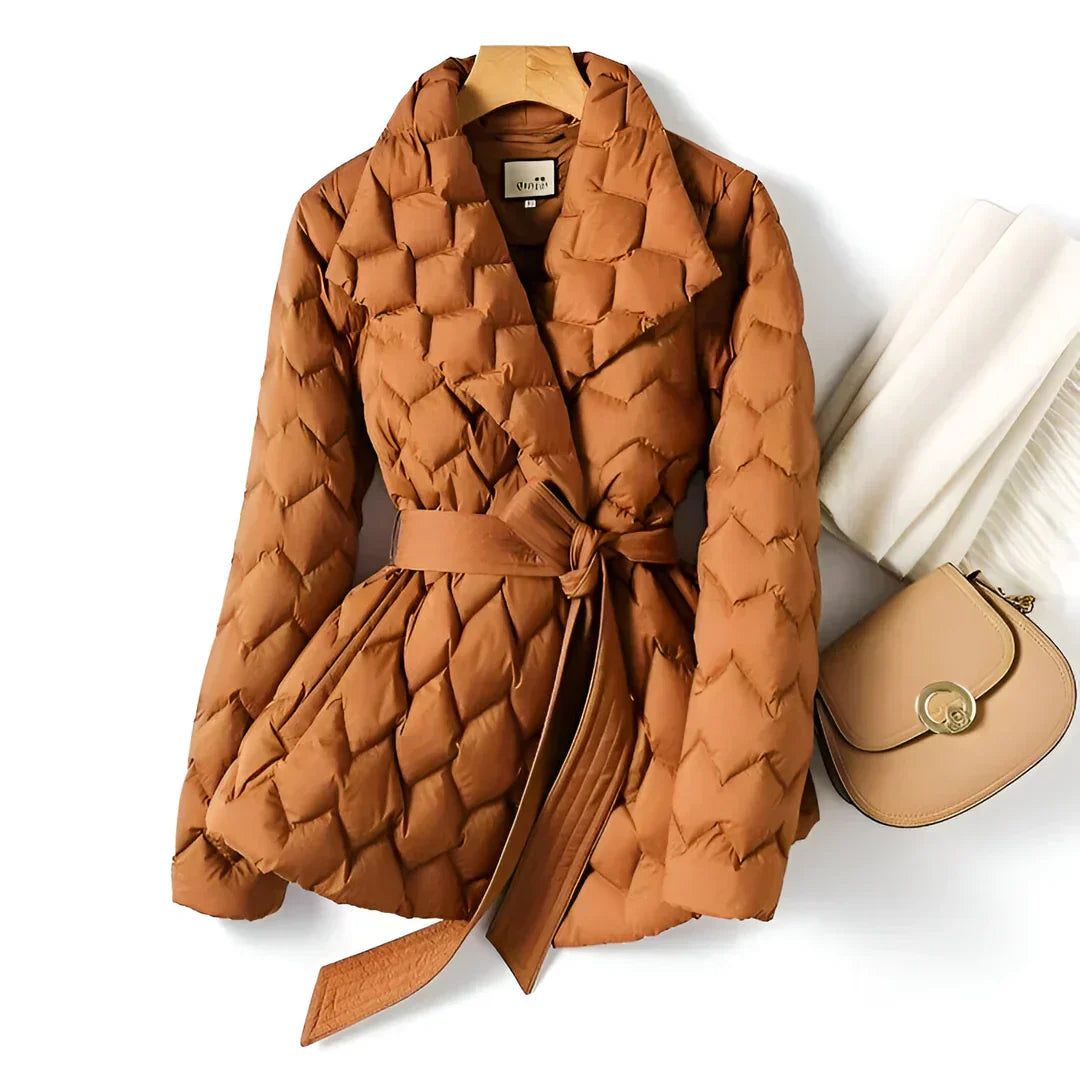 Giacca trapuntata marrone con cintura, appesa su gruccia, accanto a borsa beige e sciarpa bianca. Moda autunno inverno, abbigliamento donna elegante.