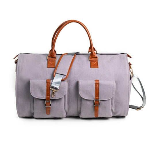 Borsone da viaggio in tela grigia con manici e dettagli in pelle marrone, tasche frontali con fibbie, tracolla regolabile. Elegante e funzionale.