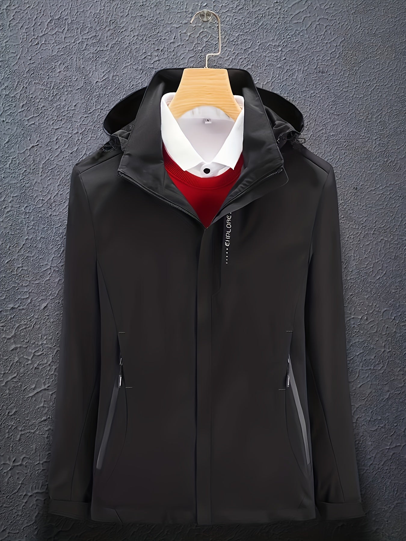 Giacca nera elegante con cappuccio, appesa su gruccia, sopra camicia bianca e maglione rosso. Moda uomo, abbigliamento invernale, stile casual.
