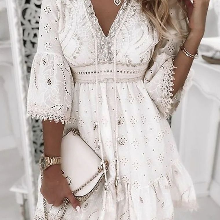 Abito bianco in pizzo con dettagli floreali, maniche a campana e scollo a V, abbinato a borsa a tracolla chiara. Look elegante e femminile.