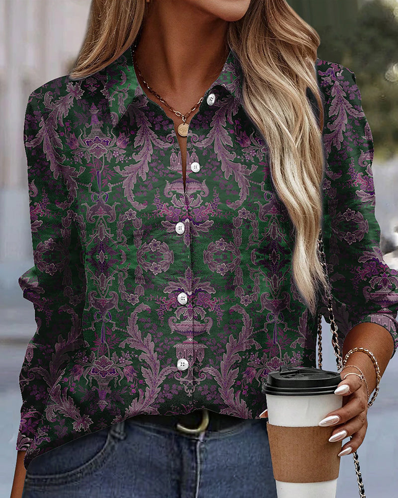 Blusa donna a maniche lunghe con motivo floreale verde e viola, abbinata a jeans. Accessori: collana dorata, borsa a tracolla, caffè da asporto.
