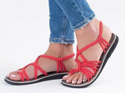 Sandali rossi intrecciati da donna, indossati con jeans. Scarpe estive eleganti, comode e alla moda. Perfette per look casual e trendy.