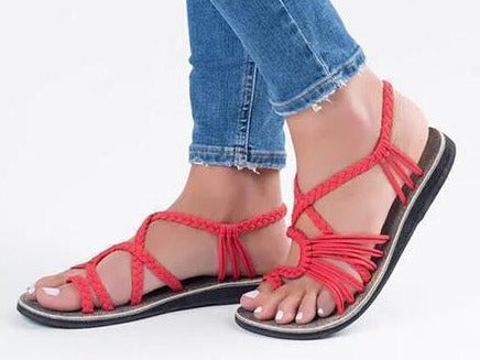 Sandali rossi intrecciati da donna, indossati con jeans. Scarpe estive eleganti, comode e alla moda. Perfette per look casual e trendy.