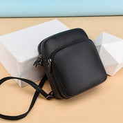 Borsa a tracolla in pelle nera su sfondo beige e azzurro, design elegante e moderno, ideale per uomo, accessorio moda, alta qualità.