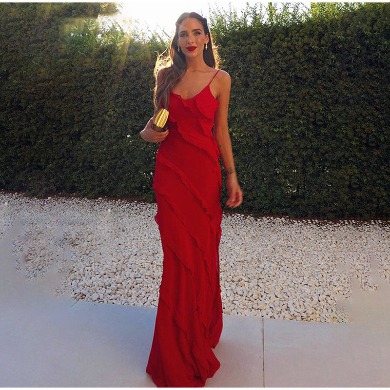 Donna in abito lungo rosso elegante, con borsa dorata, su sfondo di siepe verde. Moda serale, abbigliamento da cerimonia, stile glamour.