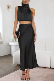 Donna in elegante abito nero satinato, top senza maniche e gonna lunga, con pochette nera. Look sofisticato per eventi serali o cerimonie.