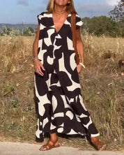 Abito lungo estivo bianco e nero con motivo astratto, indossato da donna in campagna. Moda casual, sandali marroni, stile boho chic.