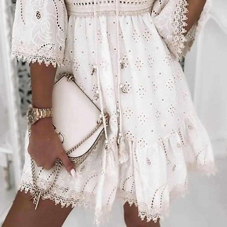 Abito estivo bianco in pizzo traforato con maniche a tre quarti, dettagli floreali e borsa a tracolla beige. Elegante moda donna estiva.