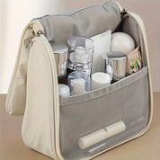 Beauty case da viaggio beige aperto, con scomparti organizzati contenenti flaconi cosmetici e accessori per la cura personale.