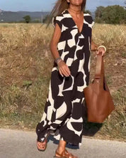 Donna con abito lungo bianco e nero astratto, borsa marrone, sandali, cammina su strada di campagna. Moda estiva, abbigliamento casual elegante.
