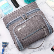 Borsa da viaggio grigia con zip multiple su sfondo di marmo, ideale per organizzare articoli da toeletta. Accessorio pratico e spazioso.