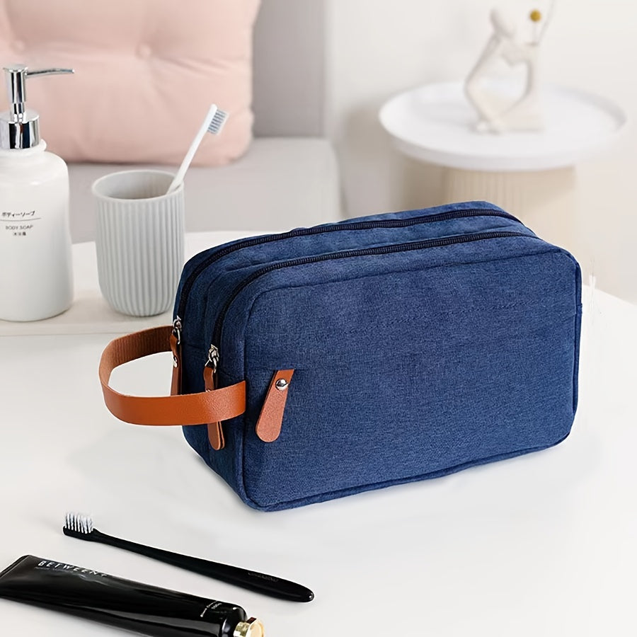 Astuccio da viaggio blu in tessuto con manico in pelle marrone, su tavolo da bagno bianco, accanto a spazzolino, dentifricio e dispenser sapone.