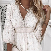 Abito bianco in pizzo con dettagli ricamati, maniche a campana, scollo a V, collana di perle, look elegante e raffinato per cerimonie o eventi speciali.