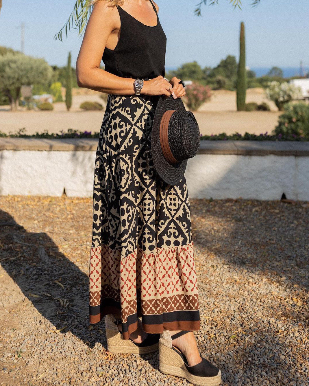 Donna con gonna lunga etnica nera e beige, top nero, sandali con zeppa, cappello di paglia. Moda estiva, abbigliamento casual elegante.