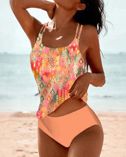 Donna in costume da bagno a due pezzi colorato su spiaggia, top con motivi geometrici e slip arancioni. Moda mare, abbigliamento estivo donna.