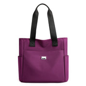 Borsa tote viola in tessuto con manici neri, tasche laterali e logo frontale. Elegante e pratica per uso quotidiano.