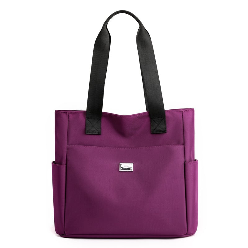 Borsa tote viola in tessuto con manici neri, tasche laterali e logo frontale. Elegante e pratica per uso quotidiano.