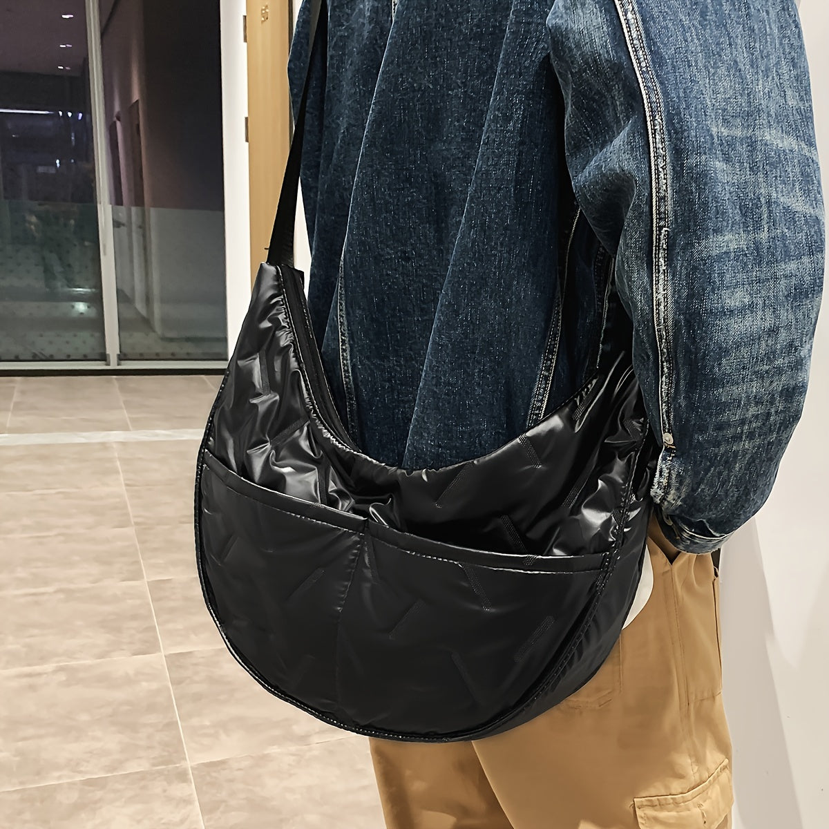 Uomo con giacca di jeans e pantaloni beige indossa borsa a tracolla nera in nylon lucido. Accessorio moda casual, stile urbano.