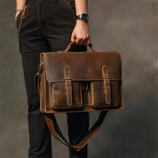 Borsa a tracolla in pelle marrone vintage, con fibbie e tasche frontali, tenuta da una persona. Elegante accessorio moda uomo.