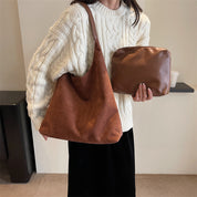 Donna con maglione bianco indossa borsa a tracolla marrone e tiene pochette in pelle marrone. Moda autunno, accessori eleganti, stile casual.