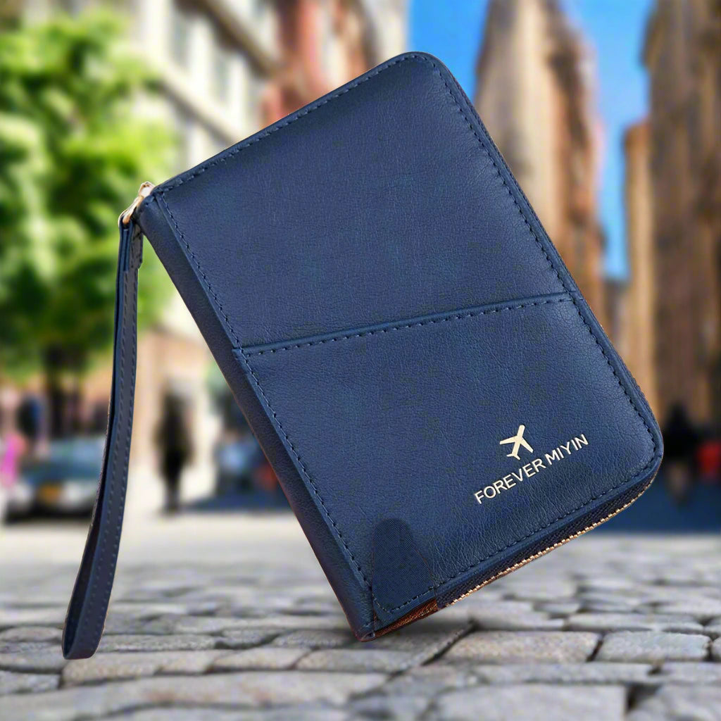 Portafoglio da viaggio blu in pelle con cerniera, logo "Forever Mwyn", sfondo urbano sfocato. Accessorio elegante e funzionale per viaggiatori.