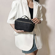 Donna con blazer bianco tiene borsa cosmetica nera scintillante con cerniera. Elegante accessorio moda, perfetto per viaggi e organizzazione trucco.