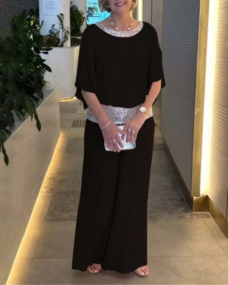 Abito elegante nero da donna con dettagli scintillanti, clutch argentata, indossato in un ambiente moderno con piante decorative.