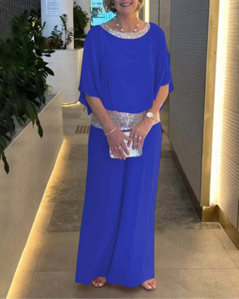 Donna in abito blu elegante con dettagli scintillanti, in piedi in un corridoio moderno. Accessori: pochette e orologio. Look da sera sofisticato.