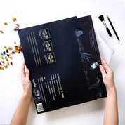 Mani che tengono un poster da grattare nero con skyline, accanto a caramelle colorate e pennelli. Kit fai-da-te artistico, regalo creativo.