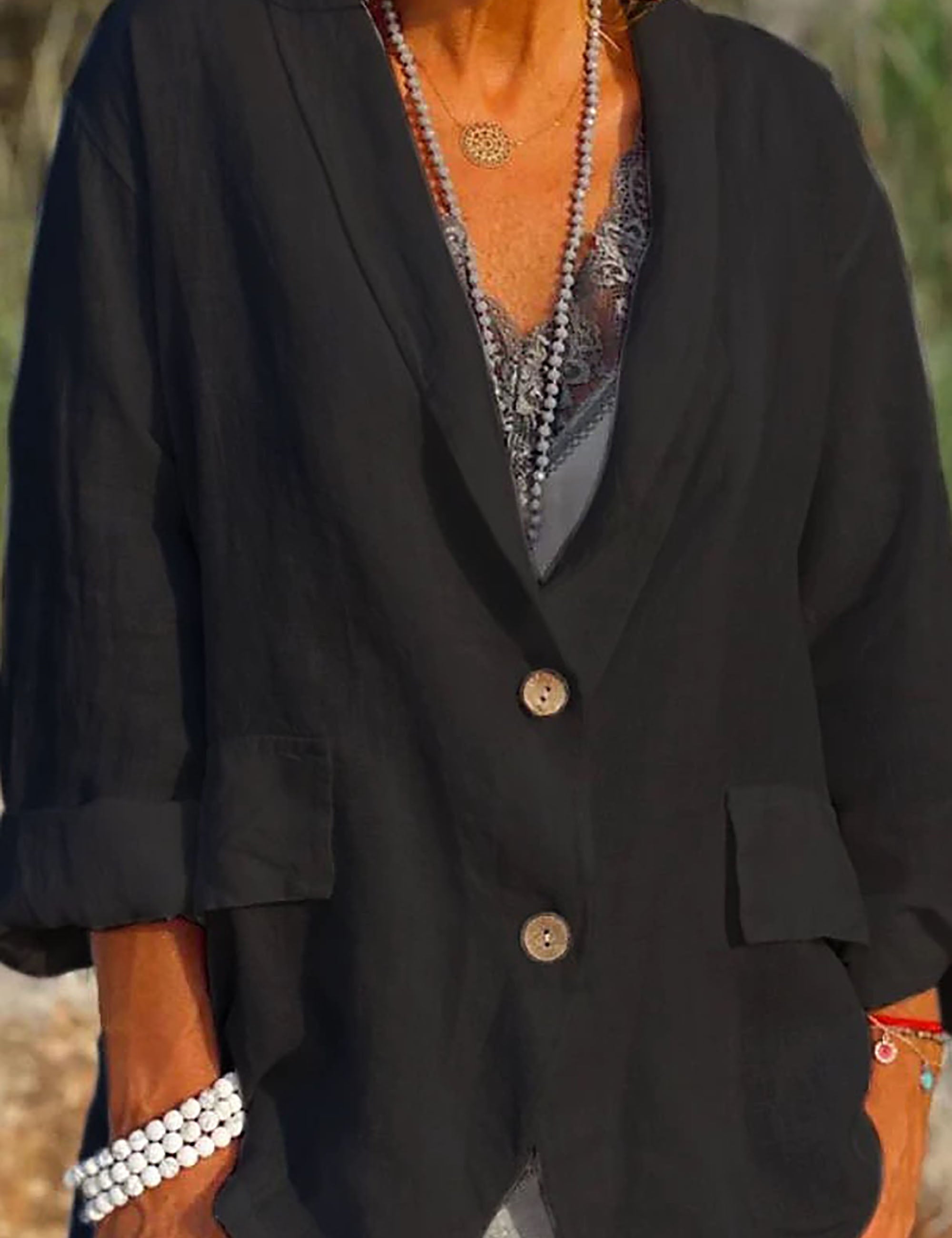 Giacca nera da donna in lino, maniche lunghe, bottoni in legno, tasche frontali, indossata con collana e bracciali. Moda casual elegante.