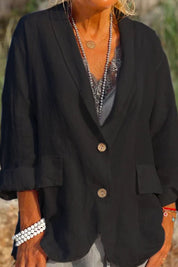 Giacca nera da donna in lino, maniche lunghe, bottoni in legno, tasche frontali, indossata con collana e bracciali. Moda casual elegante.