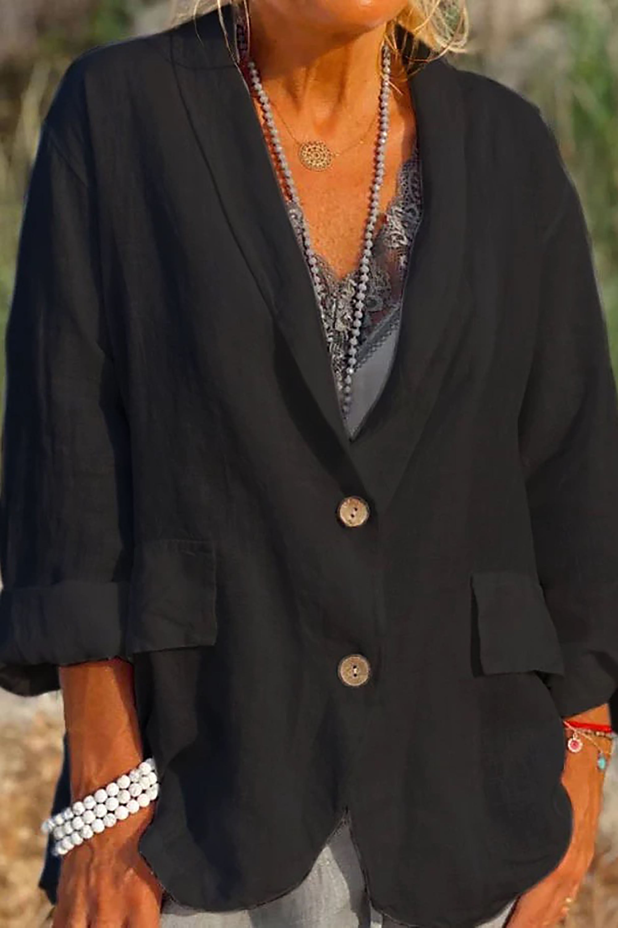 Giacca nera da donna in lino, maniche lunghe, bottoni in legno, tasche frontali, indossata con collana e bracciali. Moda casual elegante.