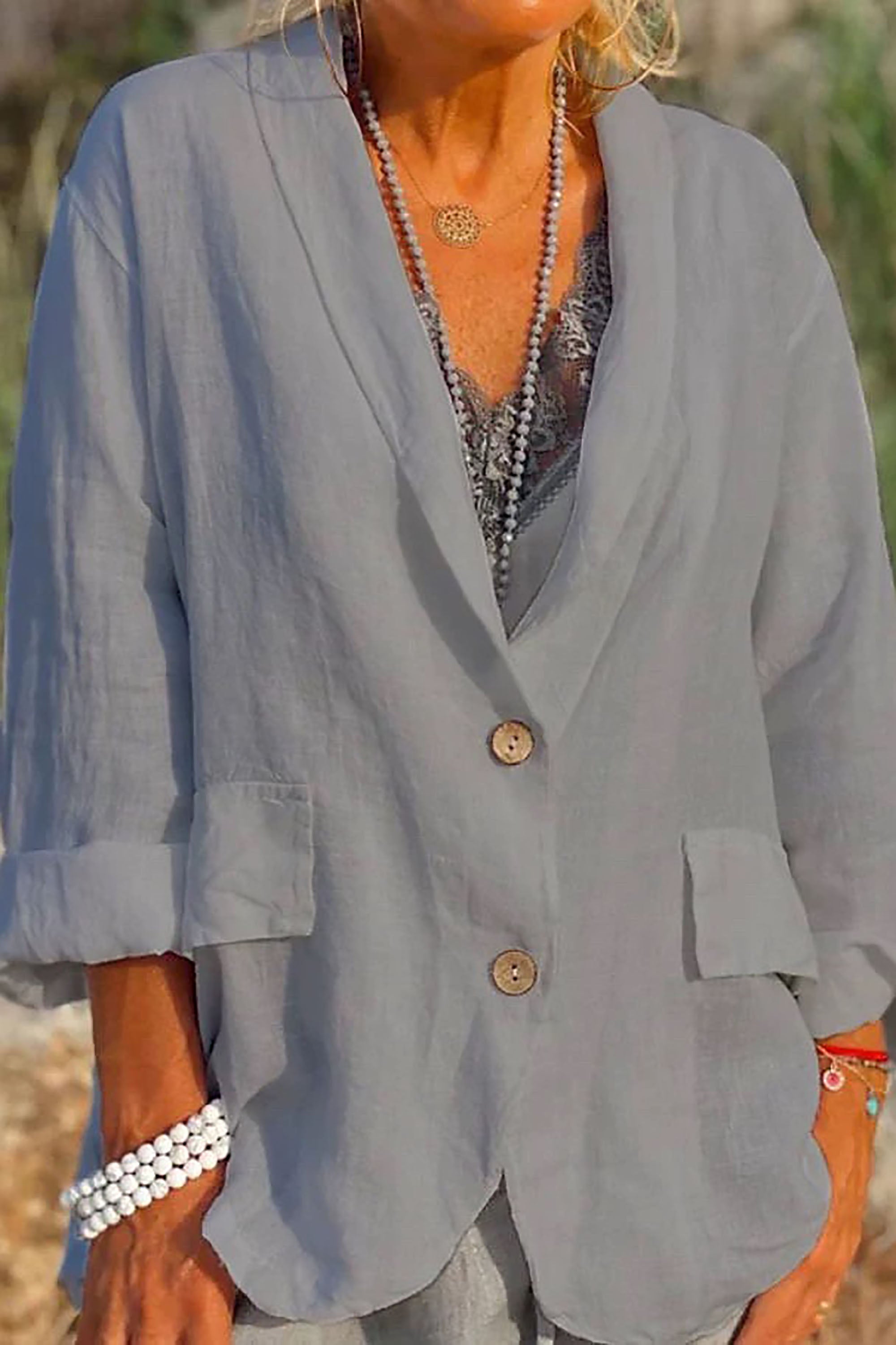 Giacca donna in lino grigio chiaro, maniche lunghe, bottoni in legno, tasche frontali, indossata sopra top in pizzo. Accessori: collana e bracciale.