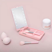 Set trucco rosa con specchio illuminato, pennelli, spugne e crema viso su sfondo rosa. Kit cosmetico portatile per make-up professionale.