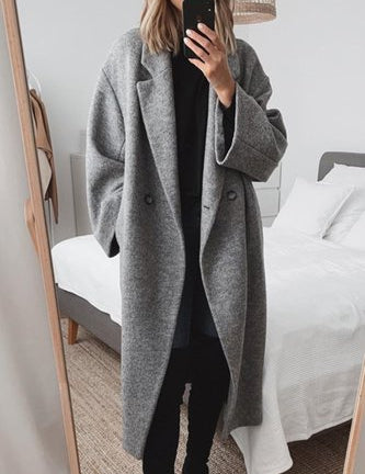 Donna in cappotto grigio oversize, scatta selfie in camera da letto moderna. Moda autunnale, abbigliamento casual elegante, tendenze 2023.