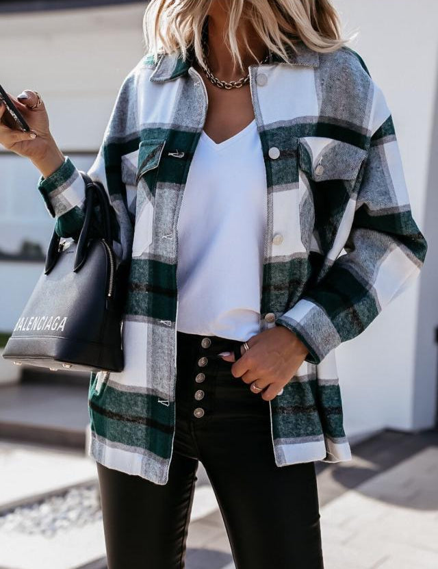 Donna con camicia a quadri verde e bianca, pantaloni neri, borsa Balenciaga, smartphone in mano. Moda autunnale casual chic.