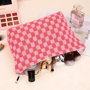 Astuccio trucco rosa a quadri con cosmetici, pennelli e profumo su sfondo chiaro. Accessori bellezza, organizzazione trucco, moda donna.