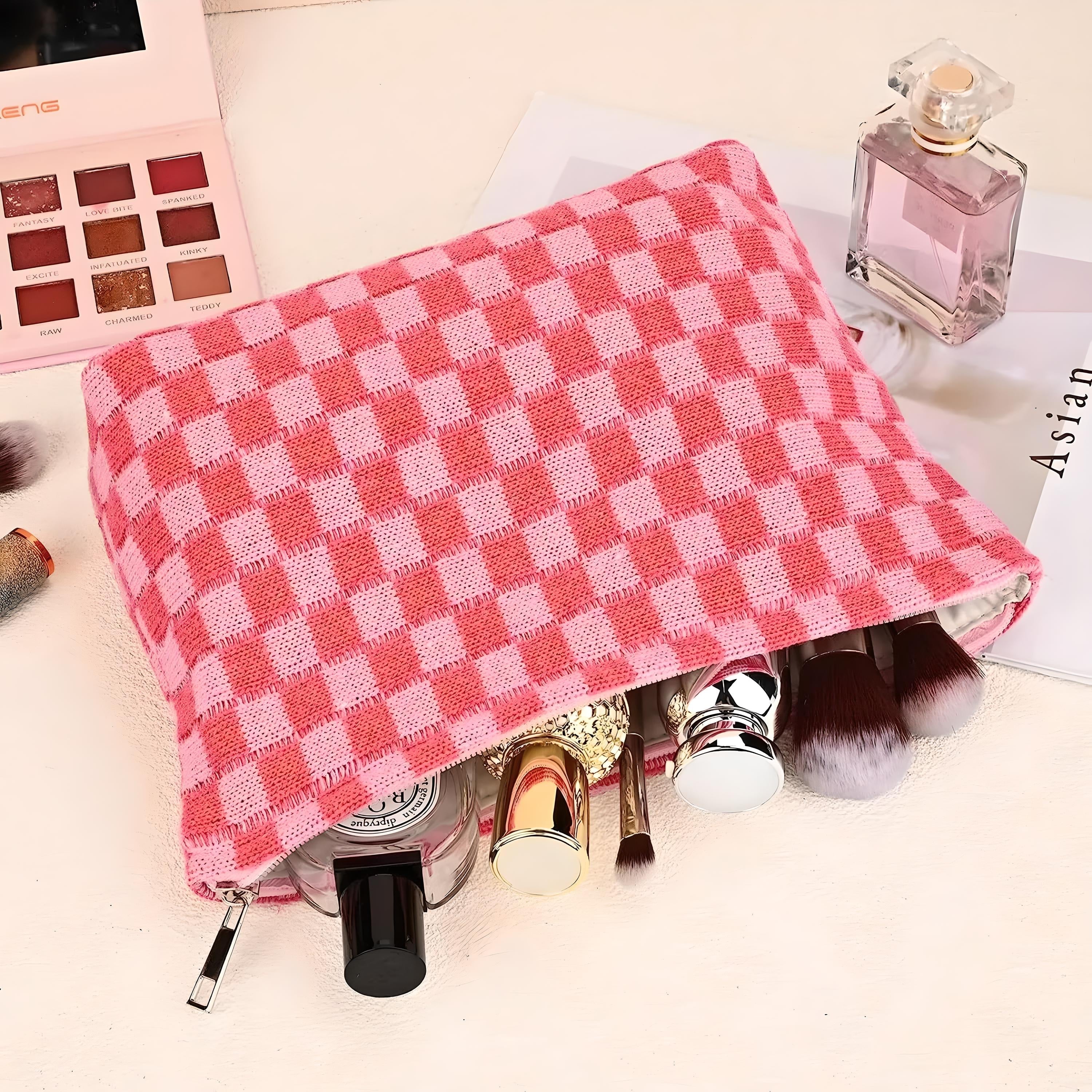 Astuccio trucco rosa a quadri con cosmetici, pennelli e profumo su sfondo chiaro. Accessori bellezza, organizzazione trucco, moda donna.