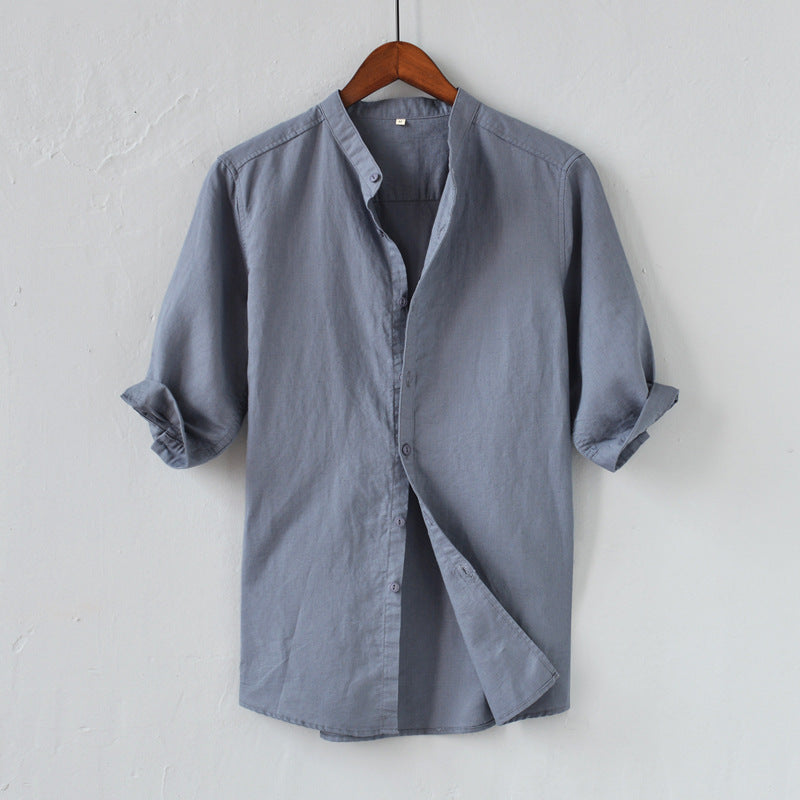 Camicia uomo grigia in cotone, maniche lunghe arrotolate, colletto alla coreana, stile casual elegante, appesa su gruccia di legno.