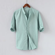 Camicia uomo verde menta, maniche lunghe arrotolate, colletto alla coreana, tessuto leggero, appesa su gruccia di legno, moda casual elegante.