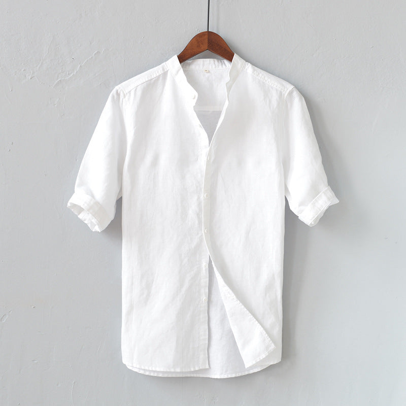 Camicia bianca in lino da uomo, maniche corte, colletto alla coreana, appesa su gruccia di legno. Elegante e casual, ideale per l'estate.