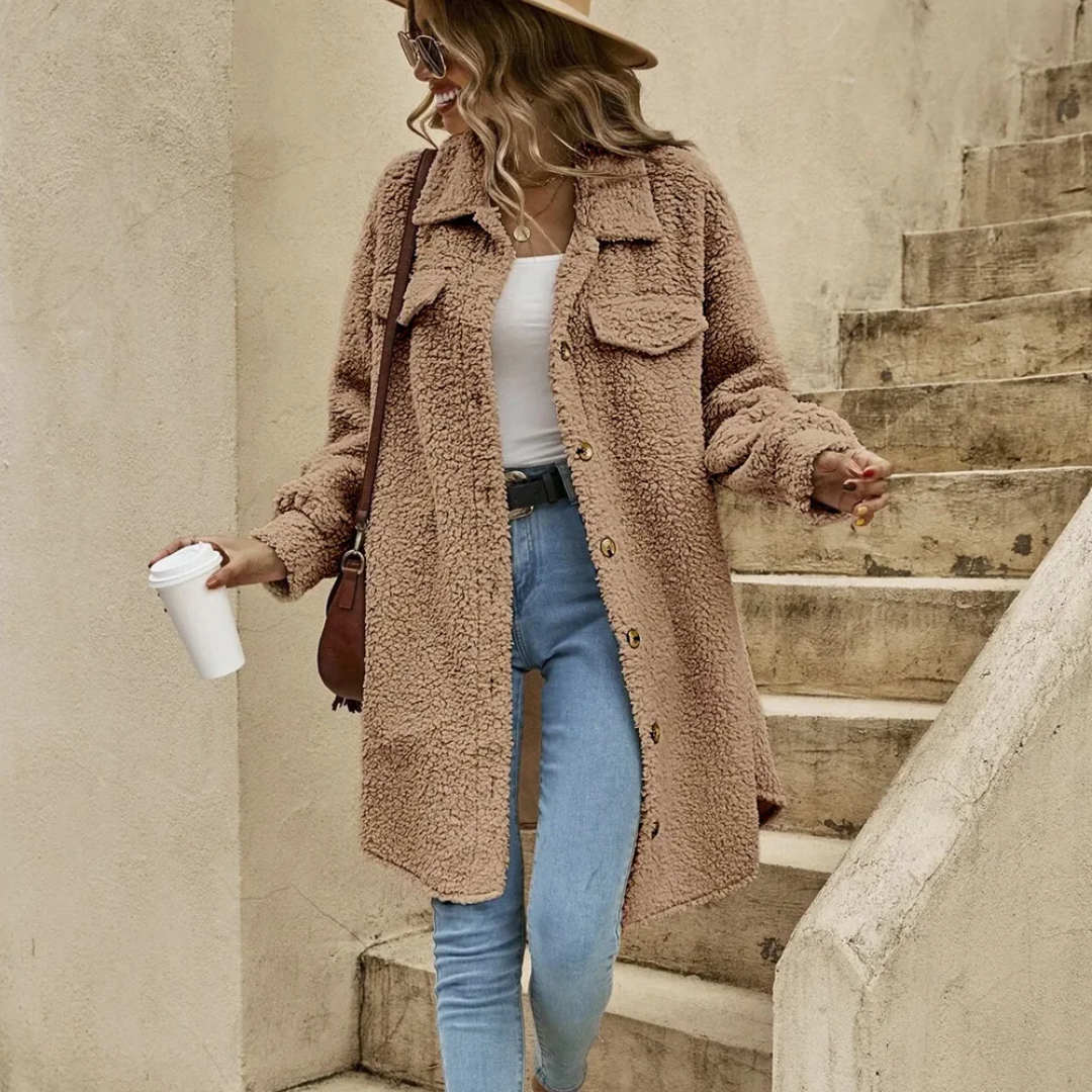 Donna con cappotto teddy beige, jeans attillati e cappello, tiene una tazza di caffè. Moda autunnale casual, stile urbano chic.