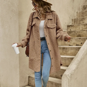 Donna con cappotto teddy beige, jeans attillati e cappello, tiene una tazza di caffè. Moda autunnale casual, stile urbano chic.
