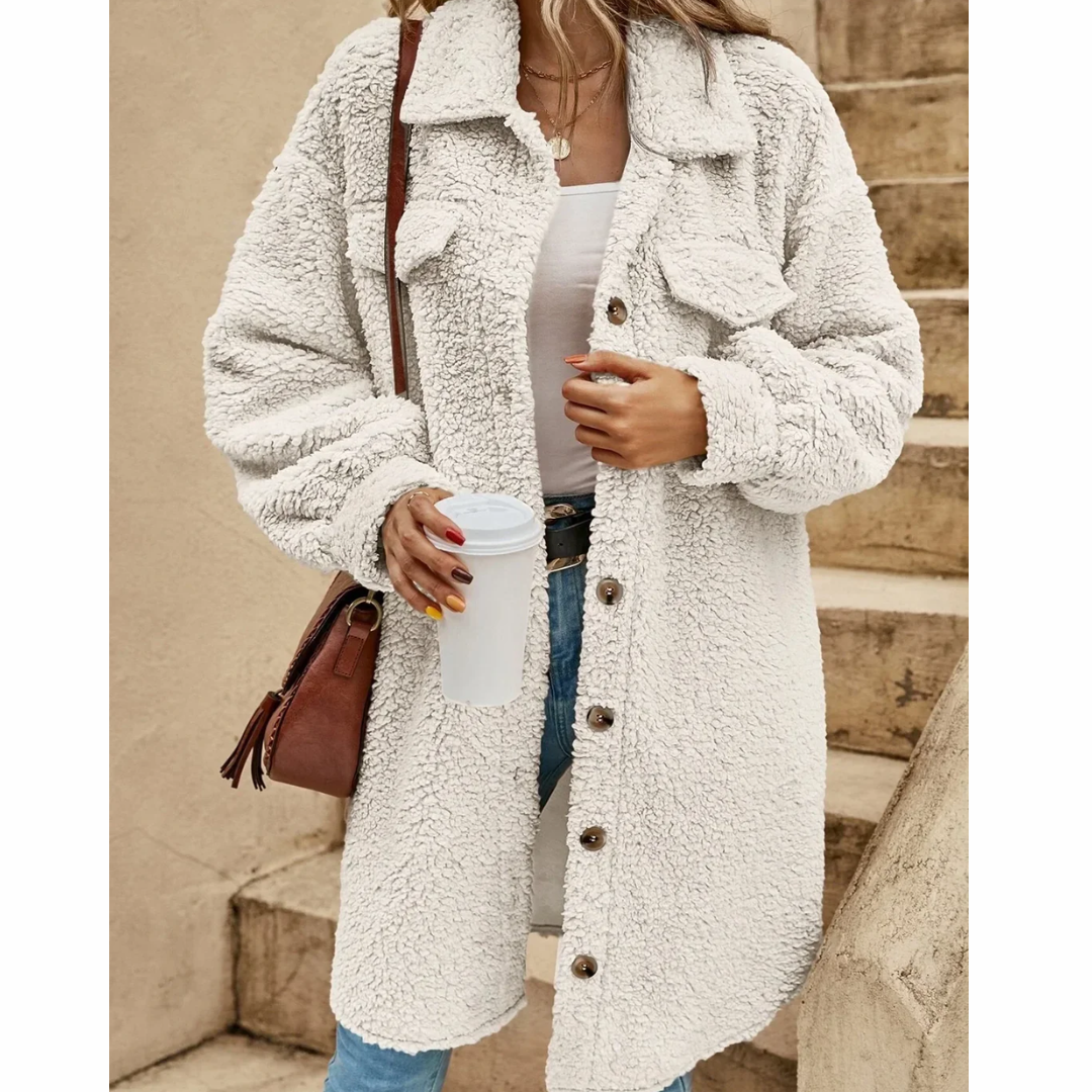 Donna con cappotto teddy bianco, borsa a tracolla marrone, jeans, e maglietta bianca, tiene una tazza di caffè. Moda autunnale casual.