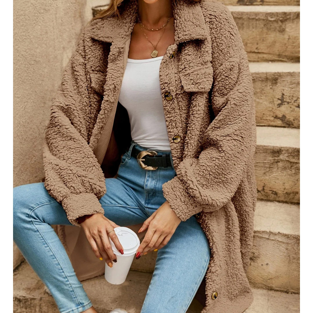 Donna con cappotto teddy beige, jeans attillati e top bianco, seduta su scale con caffè. Moda autunnale, abbigliamento casual chic.