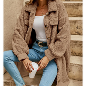 Donna con cappotto teddy beige, jeans attillati e top bianco, seduta su scale con caffè. Moda autunnale, abbigliamento casual chic.
