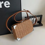 Borsa a tracolla in paglia intrecciata con angoli rinforzati in metallo e cinturino in pelle marrone, design elegante e moderno.
